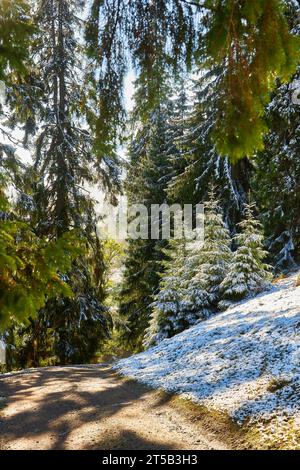 Alors que la première neige couvre la terre, un lever de soleil envoûtant peint le ciel en automne. Un sentier de montagne sinueux serpente à travers une épingle enneigée imposante Banque D'Images