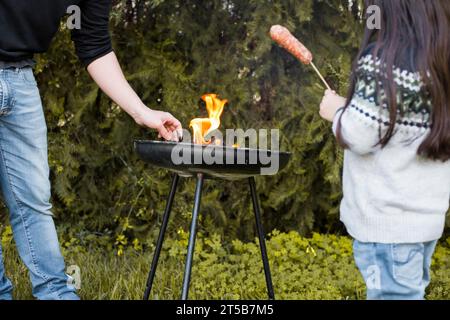 Fille avec saucisse debout près de son père grillant barbecue portable Banque D'Images