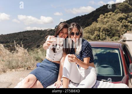 Amis féminins branchés assis voiture prenant selfie Banque D'Images