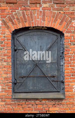 Vieille porte en métal noir sur un mur de briques rouges. Banque D'Images