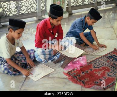 Malaisie occidentale. Malacca. Garçons locaux dans la cour de la mosquée. Lire le Coran. Banque D'Images