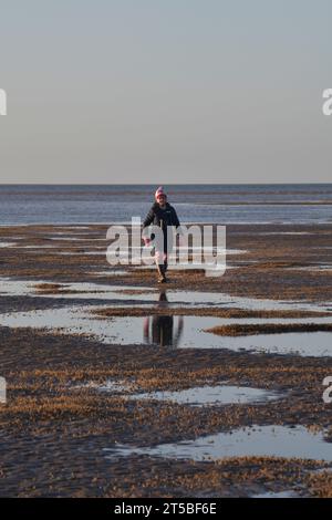 seule femme âgée marchant sur la plage à marée basse brancaster nord norfolk angleterre Banque D'Images