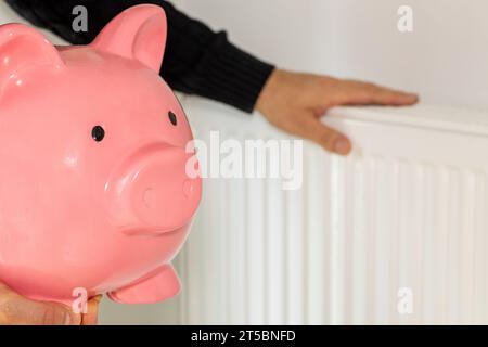 coûts de chauffage des appartements en hiver, un homme au radiateur tenant une grande tirelire dans sa main Banque D'Images