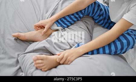 Adorable garçon assis sur le lit à la maison, gratter les pieds démangeaisons avec la main, réaction allergique de la peau causant un inconfort dans la chambre à coucher à l'intérieur Banque D'Images