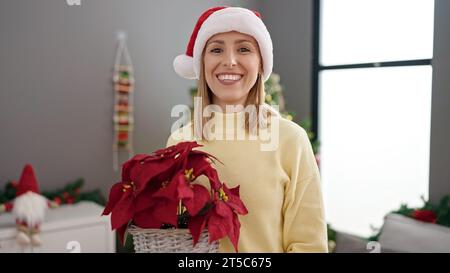 Jeune femme blonde tenant la plante debout près de l'arbre de noël à la maison Banque D'Images