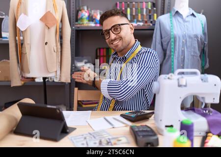 Homme hispanique avec couturier barbe travaillant à l'atelier invitant à entrer souriant naturel avec la main ouverte Banque D'Images