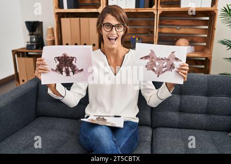 Femme Brunette travaillant avec le test rorschach à la clinique de psychologie célébrant fou et étonné de succès avec les yeux ouverts criant excité. Banque D'Images