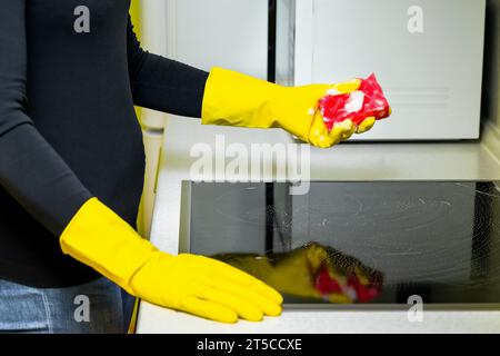 femme dans des gants en caoutchouc lave la table de cuisson dans la cuisine. laver la table de cuisson dans la cuisine. Banque D'Images