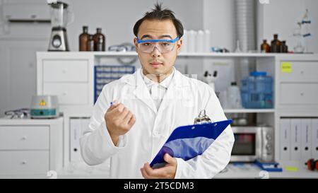 Beau, jeune, homme chinois, scientifique adulte sérieux absorbé dans l'analyse de biologie, méticuleusement prenant des notes sur le presse-papiers tout en parlant passionnément Banque D'Images