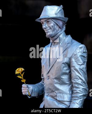 Homme peint en argent avec une rose en or prétendant être une statue se produisant à Edinburgh Fringe, en Écosse Banque D'Images
