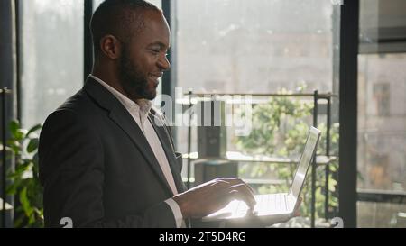 Homme senior mature homme d'affaires ethnique afro-américain travailleur adulte stand dans le bureau de l'entreprise avec le travail exécutif masculin de fond de soleil d'ordinateur portable Banque D'Images