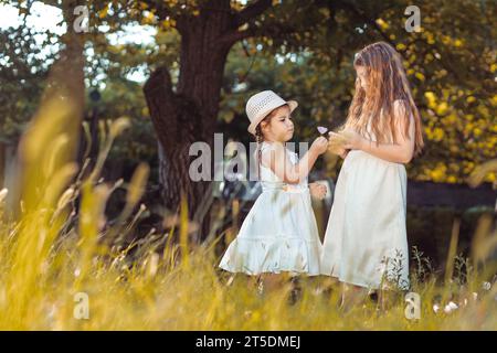 Deux petites filles, sœurs en robes blanches cueillant des fleurs dans la nature Banque D'Images