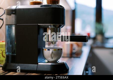 Café coulant du porte-filtre d'une machine à café à caroube dans une tasse sur un support Banque D'Images