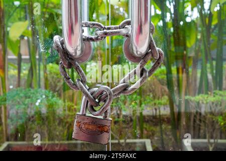 Photo en gros plan d'une chaîne en fer et d'un cadenas en fer sur une porte en verre Banque D'Images