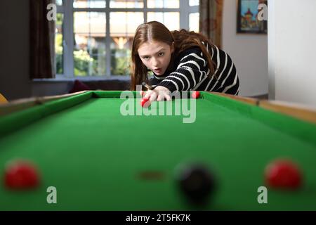 Adolescente frappant un coup de feu au jeu traditionnel de bagatelle dans le salon à la maison, avec table de Baize verte Banque D'Images