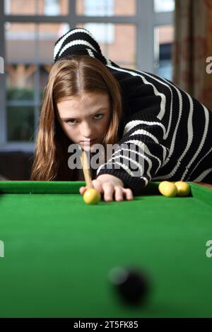 Adolescente jouant au jeu traditionnel de pub de bagatelle dans le salon à la maison, alignement de tir avec cue Banque D'Images