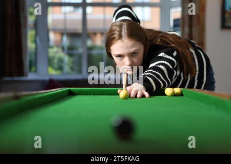 Adolescente jouant au jeu traditionnel de pub de bagatelle dans le salon à la maison montrant une détermination féroce et l'attention. Banque D'Images