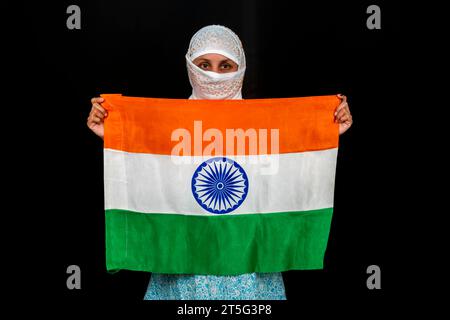 Jeune femme indienne tenant Tricolor dans ses mains, drapeau de l'Inde, isolé sur fond noir Banque D'Images