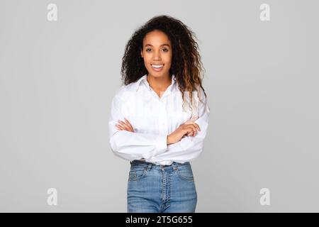 Heureuse dame noire pose avec confiance les mains croisées, fond gris Banque D'Images