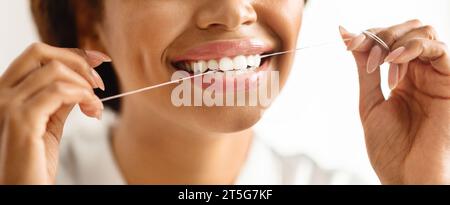 Cliché recadré de femme noire souriante utilisant Dental Floss at Home Banque D'Images