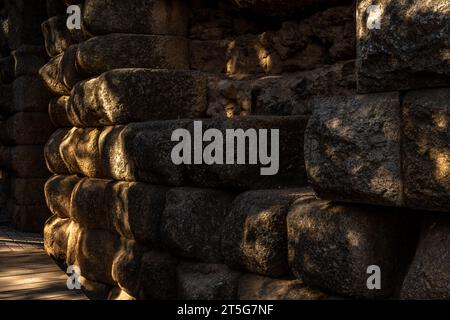 Blocs de pierre et de roche du mur entourant les escaliers de l'ancien théâtre romain de Mérida, avec la porte voûtée en arrière-plan illuminée Banque D'Images