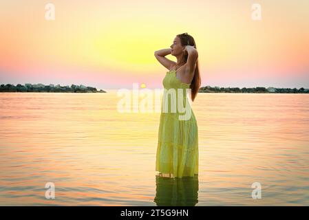 Une jeune femme défrisant ses cheveux rencontre le lever du soleil, allant dans la mer. Banque D'Images