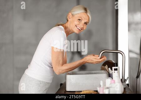 Belle femme mature laver le visage dans l'intérieur de la salle de bains Banque D'Images