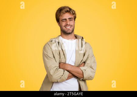 Jeune homme européen aux bras pliés, souriant et claquant sur fond jaune Banque D'Images