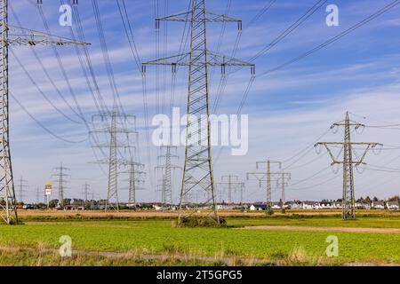 D'innombrables pylônes à haute tension et lignes électriques dans la nature devant les maisons d'une ville en arrière-plan Banque D'Images