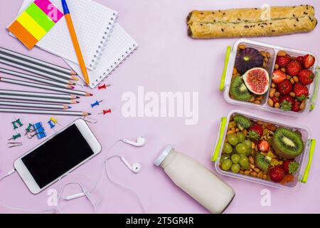 Boîte à lunch équilibrée saine. Ensemble de fruits, baies légumes Pie. Bouteille de yaourt. Téléphone avec casque. Bureau rose. Pose à plat. Nourriture de bureau, déjeuner HEA Banque D'Images