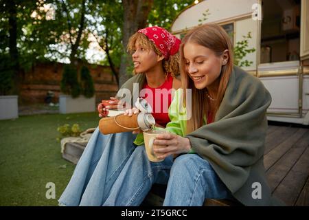 Deux amies féminines attrayantes buvant du thé chaud profitant des vibrations de camping d'été Banque D'Images