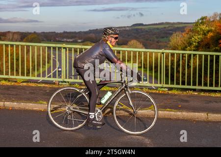 Cycliste féminine cycliste spécialisée Roubaix fibre de carbone vélo de route sportive sur la route de campagne traversant le pont autoroutier dans le Lancashire rural, Royaume-Uni Banque D'Images