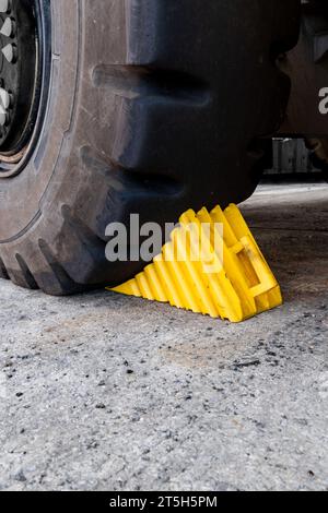 Une cale de roue jaune pour usage intensif calée contre un pneu du véhicule comme mesure de sécurité pour empêcher le véhicule de rouler avec un espace de copie Banque D'Images