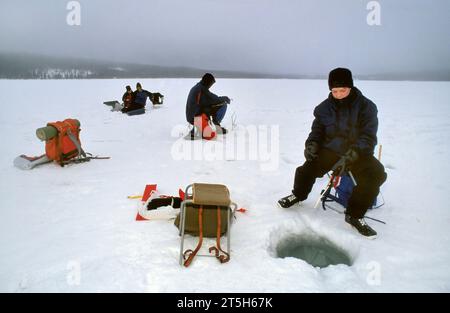 TROMSO, NORVÈGE - JANVIER 14 2022 : pêcheurs pêchant sur glace sur un lac gelé en hiver avec canne à pêche ou canne à pêche, tarière à glace et équipement pour la pêche Banque D'Images