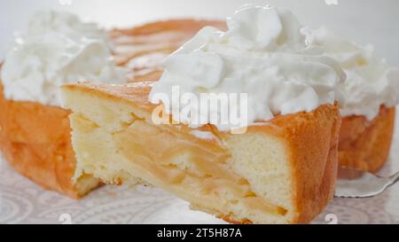 Couper en tranches un gâteau aux pommes fraîchement cuit avec de la crème fouettée en gros plan. Chef servant un gâteau Banque D'Images