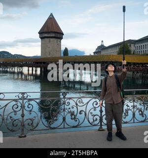 Lucerne, Suisse - 26 août 2023 : un touriste asiatique concentré prend un selfie par mauvais temps devant le pont de la Chapelle Banque D'Images