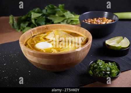 Plat typiquement péruvien connu sous le nom de soupe au poulet, dans un bol en bois avec citron et ciboulette. Banque D'Images