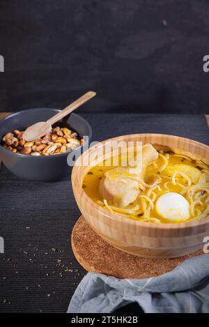 Plat typiquement péruvien connu sous le nom de soupe au poulet, dans un bol en bois avec citron et ciboulette. Banque D'Images