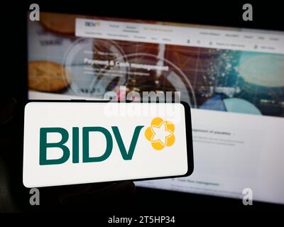 Personne tenant le téléphone portable avec le logo de la Banque commerciale pour l'investissement et le développement du Vietnam en face de la page Web. Concentrez-vous sur l'affichage du téléphone. Banque D'Images