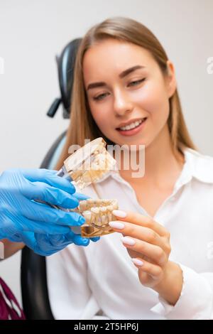 Un dentiste, ganté et préparé, tient un modèle de mâchoire humaine pour élucider une approche de traitement pour un patient Banque D'Images