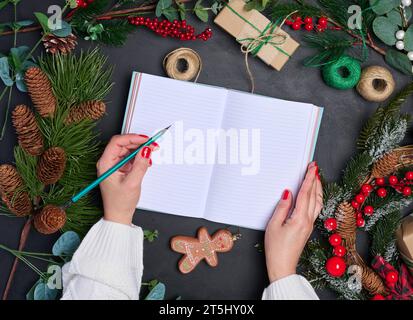 Une femme est assise à une table entourée de décorations et de cadeaux de Noël. Elle écrit dans un bloc-notes, vue de dessus Banque D'Images