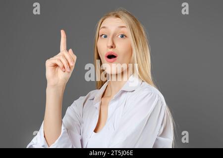 Jeune femme intelligente a trouvé une solution et pointe son doigt vers le haut pour attirer l'attention Banque D'Images