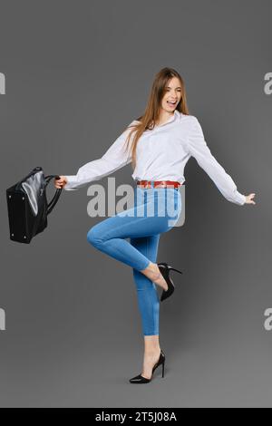 Femme joyeuse agitant ses bras tout en tenant un sac et debout sur une jambe Banque D'Images