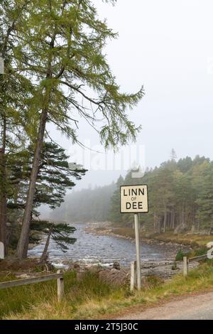 Le panneau routier 'Linn of Dee', avec la rivière Dee et les forêts de pins dans la brume d'automne en arrière-plan Banque D'Images