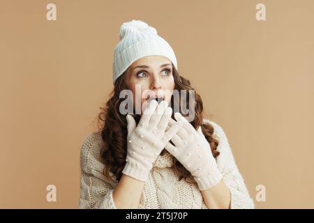 Bonjour l'hiver. surprise femme d'âge moyen tendance en pull beige, mitaines et chapeau isolé sur beige. Banque D'Images