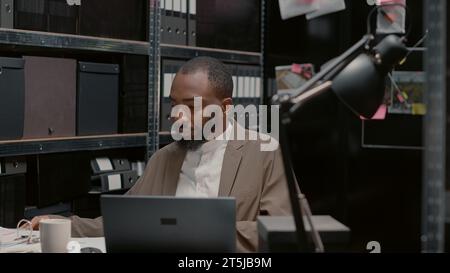 Inspecteur recherchant des preuves médico-légales dans le dossier de l'affaire, analysant des indices pour mener une enquête criminelle. Détective privé examinant les photos de surveillance pour des indices, bureau de police professionnel. Banque D'Images