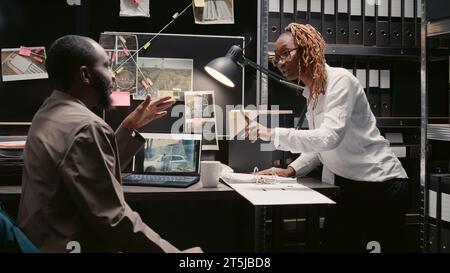 Agents afro-américains analysant des rapports de cas au bureau, travaillant sur des enquêtes criminelles. Équipe d'inspecteurs lisant les déclarations de témoins dans les archives de la police, regardant la carte de détective. Banque D'Images