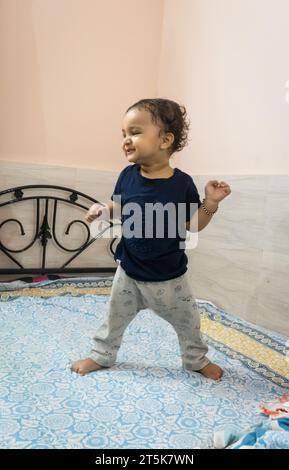 mignon bébé garçon en bas âge essayant de se tenir debout pour la première fois au lit à la maison Banque D'Images