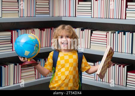 Pupille excitée. Garçon d'école avec globe du monde et échecs, enfance. Petit écolier. Portrait d'élève nerd avec des fournitures scolaires. Banque D'Images