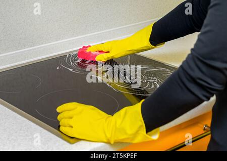 femme dans des gants en caoutchouc lave la table de cuisson dans la cuisine. laver la table de cuisson dans la cuisine. Banque D'Images